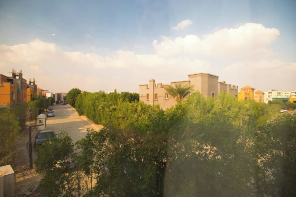 A residential street with houses, trees, and parked cars.