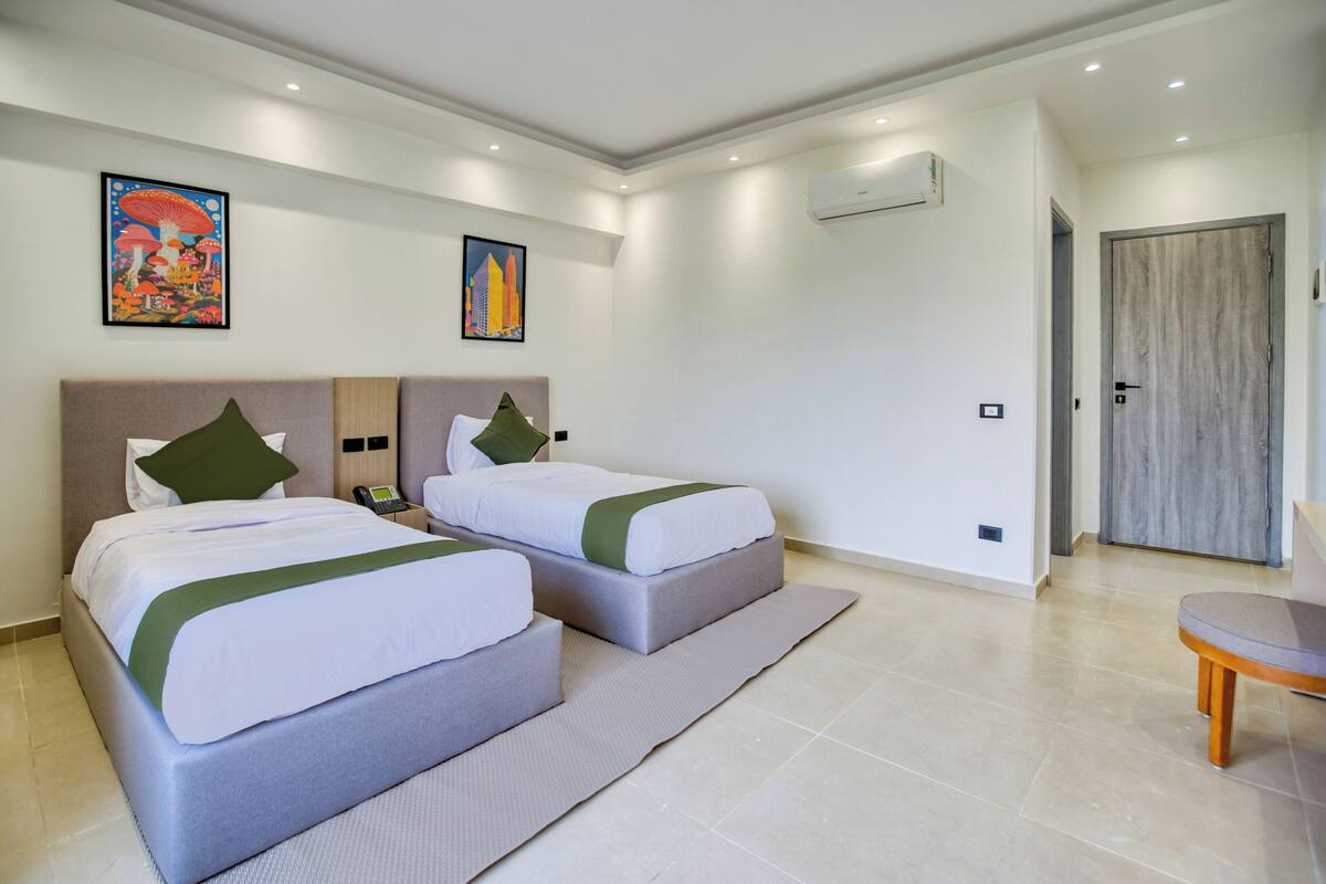 A hotel room with two beds, a small table, and artwork on the walls.