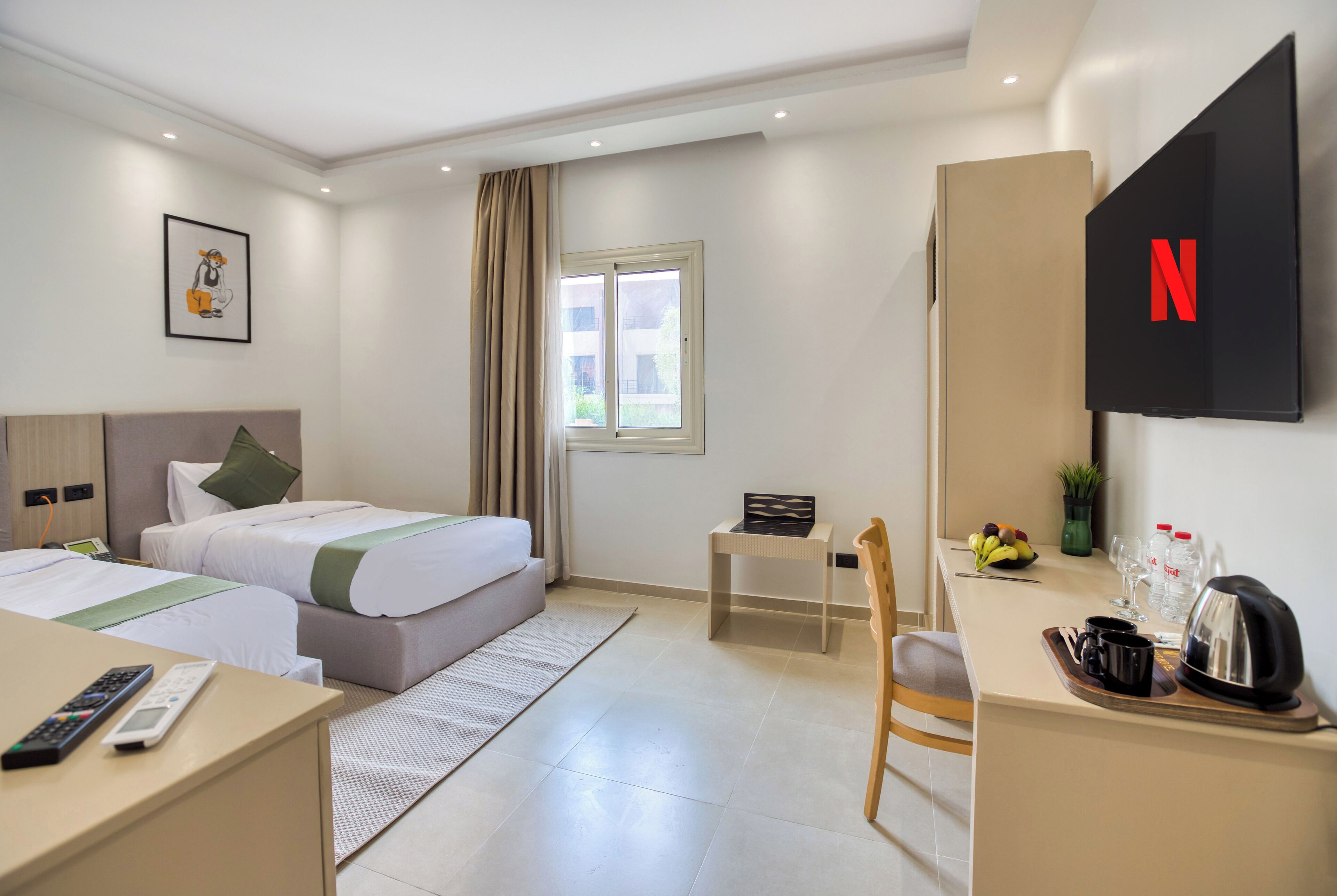 A hotel room with two beds, a desk, a chair, a TV, and a window with curtains.