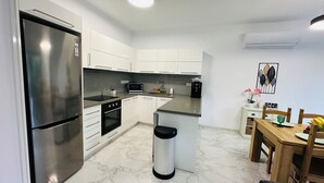 A modern kitchen with a stainless steel refrigerator, a microwave, an oven, and a sink. There is a wooden dining table with chairs and a small island with a sink.