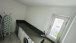 A compact kitchen with a washing machine, a sink, and a window with a view of buildings.
