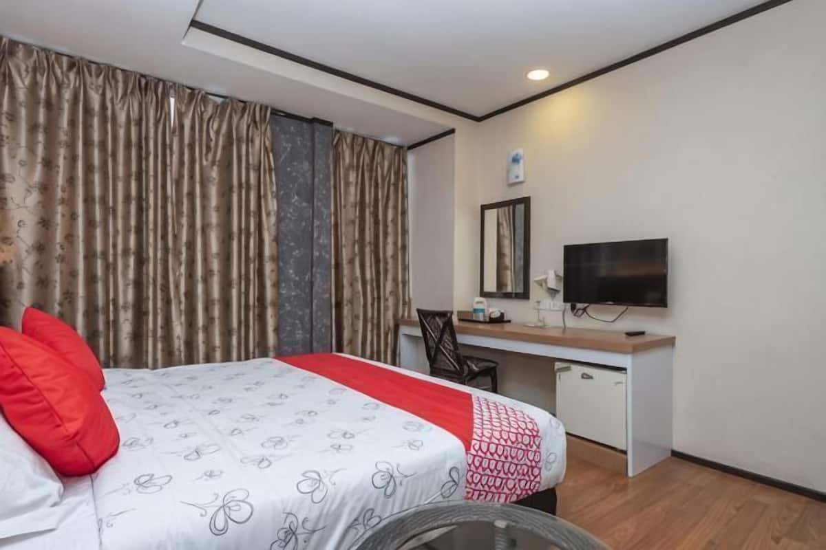 Een hotelkamer met een bed, bureau, stoel, televisie en gordijnen.