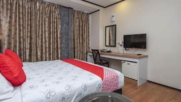 Quarto de hotel com cama, escrivaninha, cadeira, televisão e cortinas.