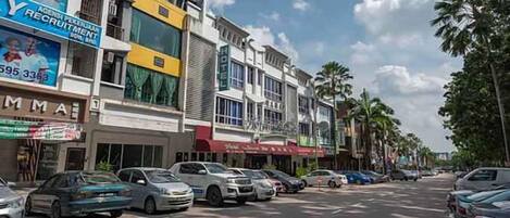 A street view with parked cars, buildings with various signs, and palm trees.