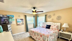 Une chambre à coucher avec un lit, un ventilateur de plafond, une télévision et un bureau.