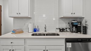 A modern kitchen with white cabinets, a stainless steel sink, and a coffee maker. - 3BR Walkable Downtown Retreat ~ King Bed + Porch (Salisbury)