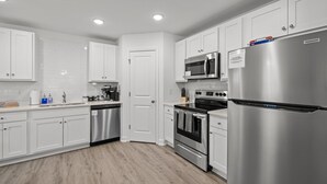 A modern kitchen with white cabinets, stainless steel appliances, and a wooden floor. - 3BR Walkable Downtown Retreat ~ King Bed + Porch (Salisbury)