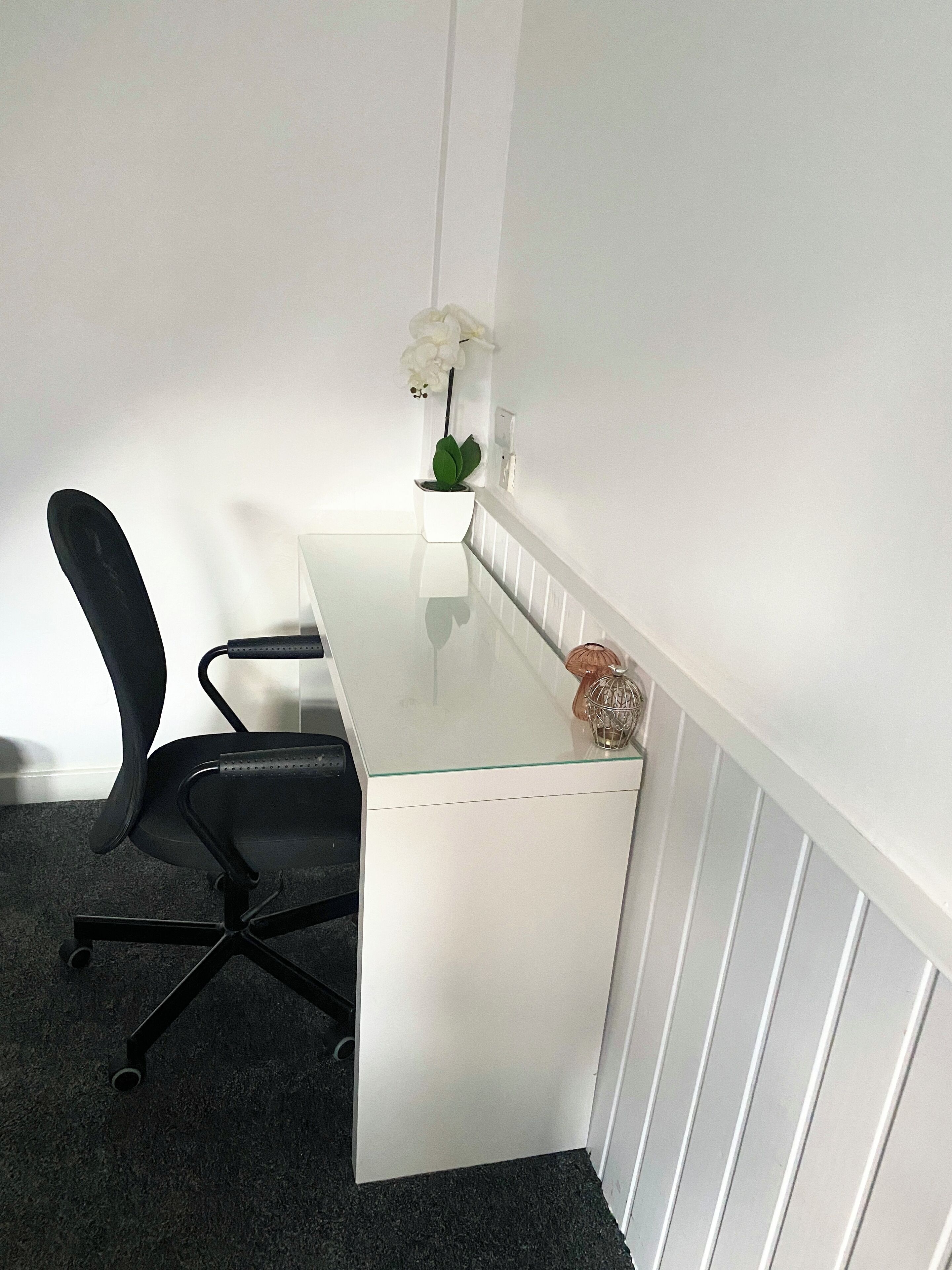 Una sala de conferencias con una mesa blanca, una silla de oficina negra y una orquídea en maceta.