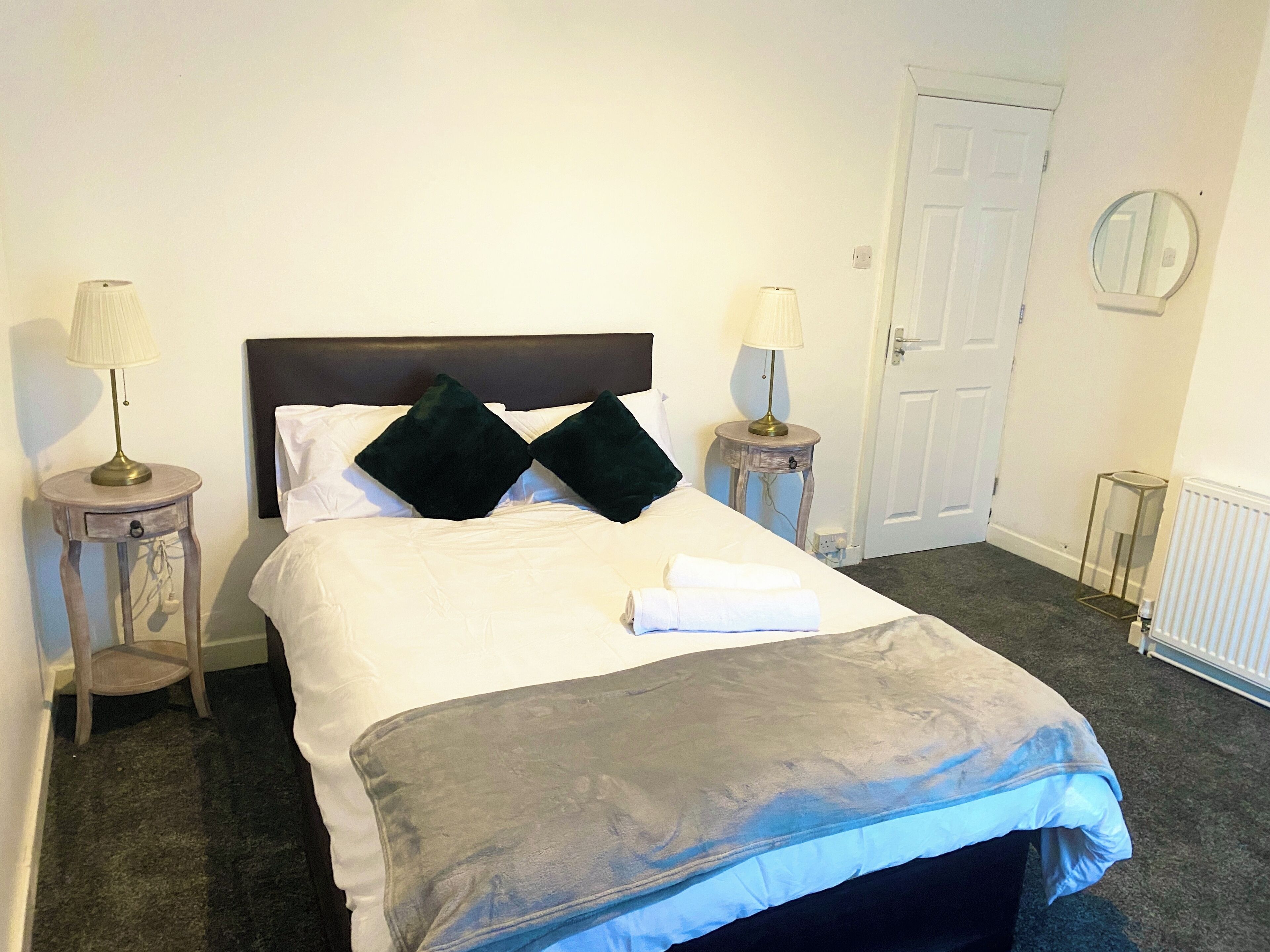 A neatly made bed with a grey and blue blanket, two dark pillows, and two bedside lamps on wooden nightstands.