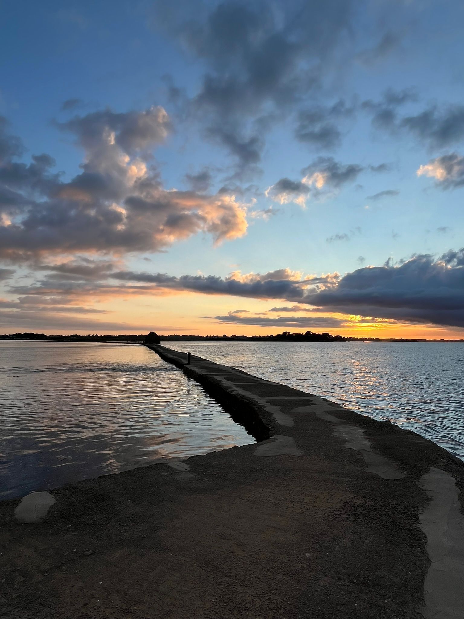 A concrete walkway extending into a body of water with a sunset in the background.