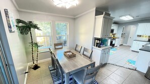 Una cucina moderna con mobili bianchi, una zona pranzo con tavolo e sedie in legno e un'ampia finestra vista giardino.