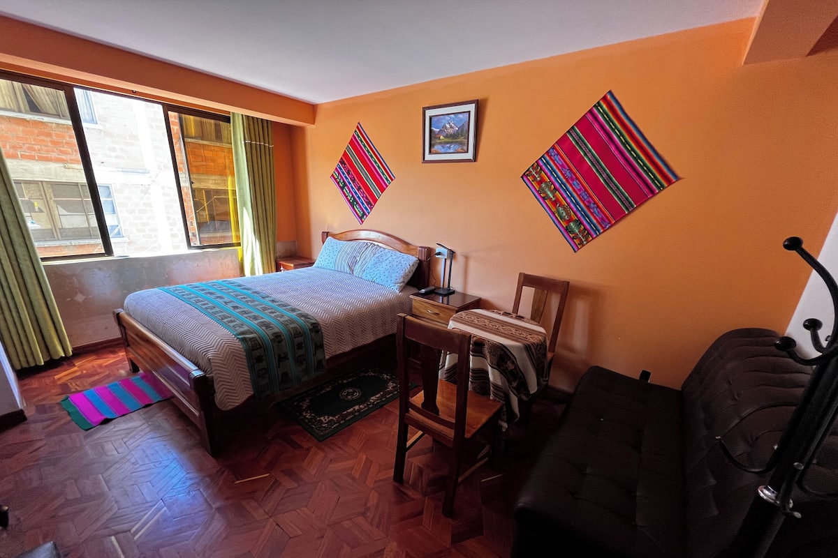 A bedroom with a bed, a desk, a chair, and a window.