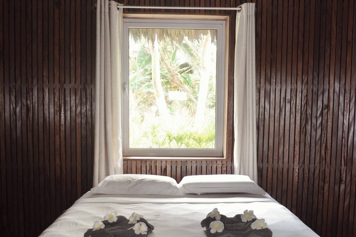 A bed with white linens, a window with curtains, and a ceiling fan.