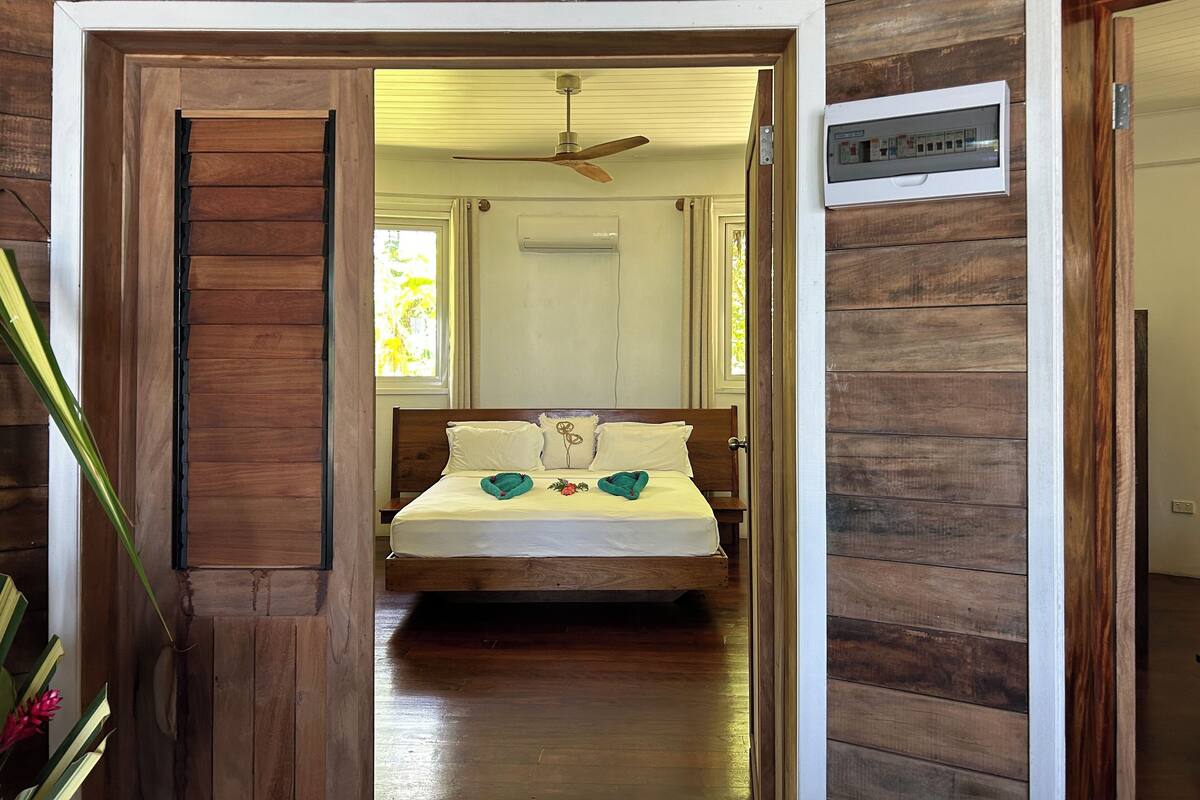 A wooden room with a bed, a ceiling fan, and a window.