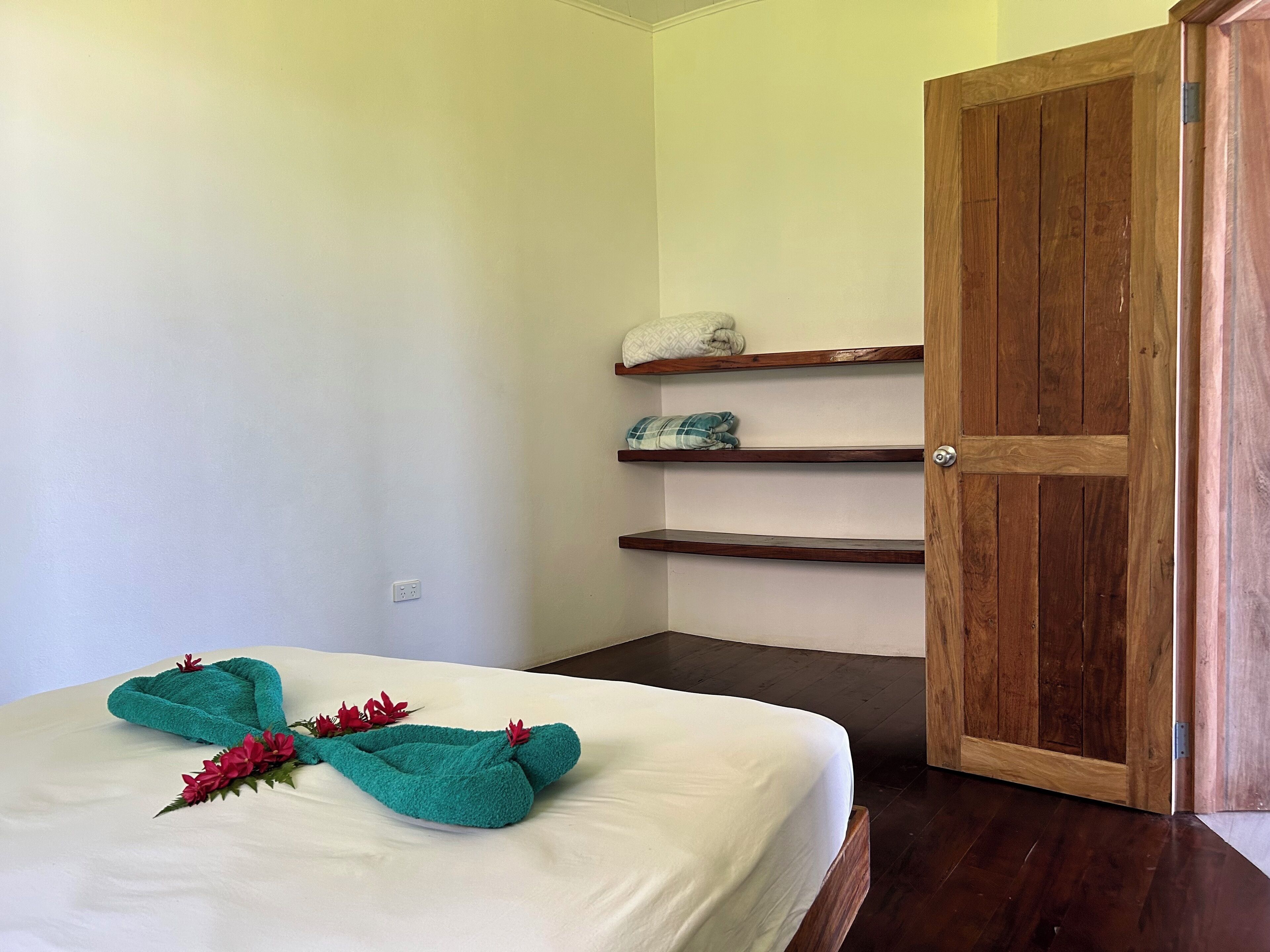 A bedroom with a bed, wooden door, and shelves with folded towels.