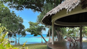 A wooden deck with a thatched roof, overlooking a beach with clear blue water and lush greenery. - Black Pearl Resort  (Saraotou)