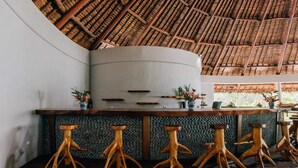 A bar area with a curved counter, wooden stools, and a thatched roof ceiling. - Black Pearl Resort  (Saraotou)