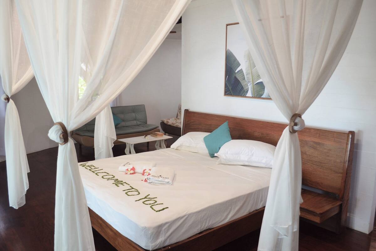 A bed with a canopy, a bedside table, a chair, and a small table with a lamp.