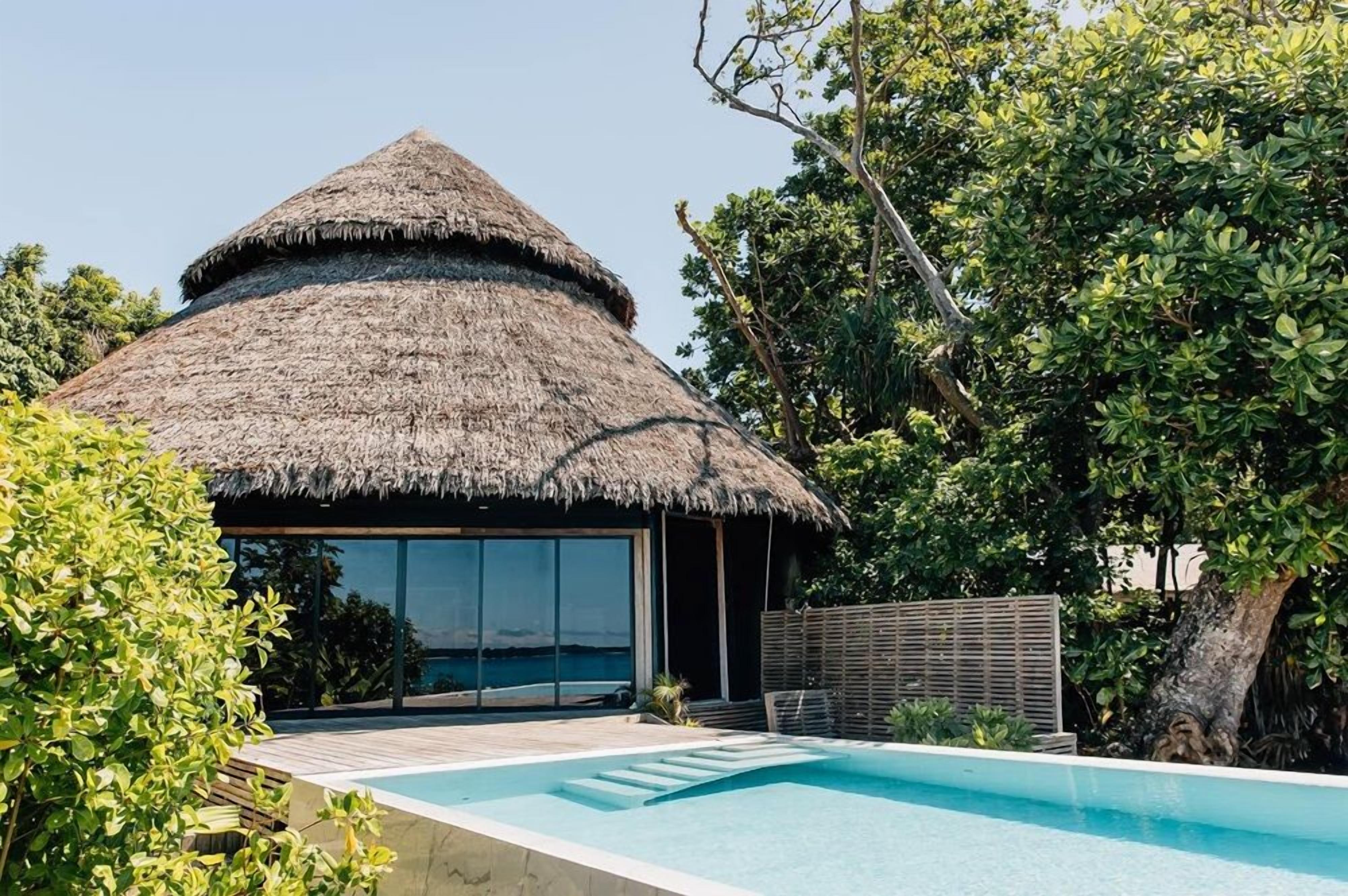 Una estructura con techo de paja, una piscina y vistas al mar.