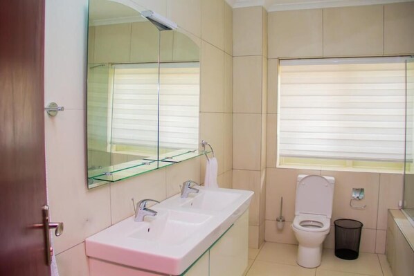 A modern bathroom with a glass-fronted sink, a toilet, and a trash bin.
