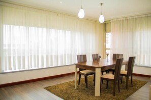 A dining area with a wooden table and chairs, large windows with sheer curtains, and hanging pendant lights.
