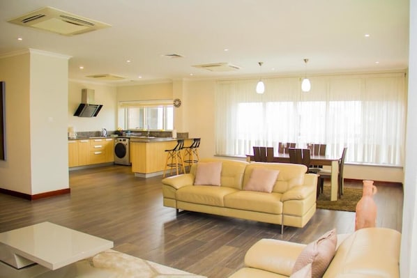 A modern living room with a sofa, a dining table, and a kitchen in the background.
