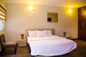 A bedroom with a large bed, two bedside tables, a chair, and a mirror on the wall.