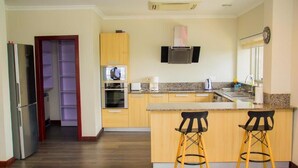 Cocina moderna con gabinetes de madera, refrigerador de acero inoxidable, microondas y horno integrado. Hay dos taburetes de bar en la isla.