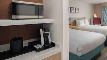 A hotel room with a microwave, coffee maker, and a small table with cups. There are two beds with white bedding and a nightstand with a lamp.