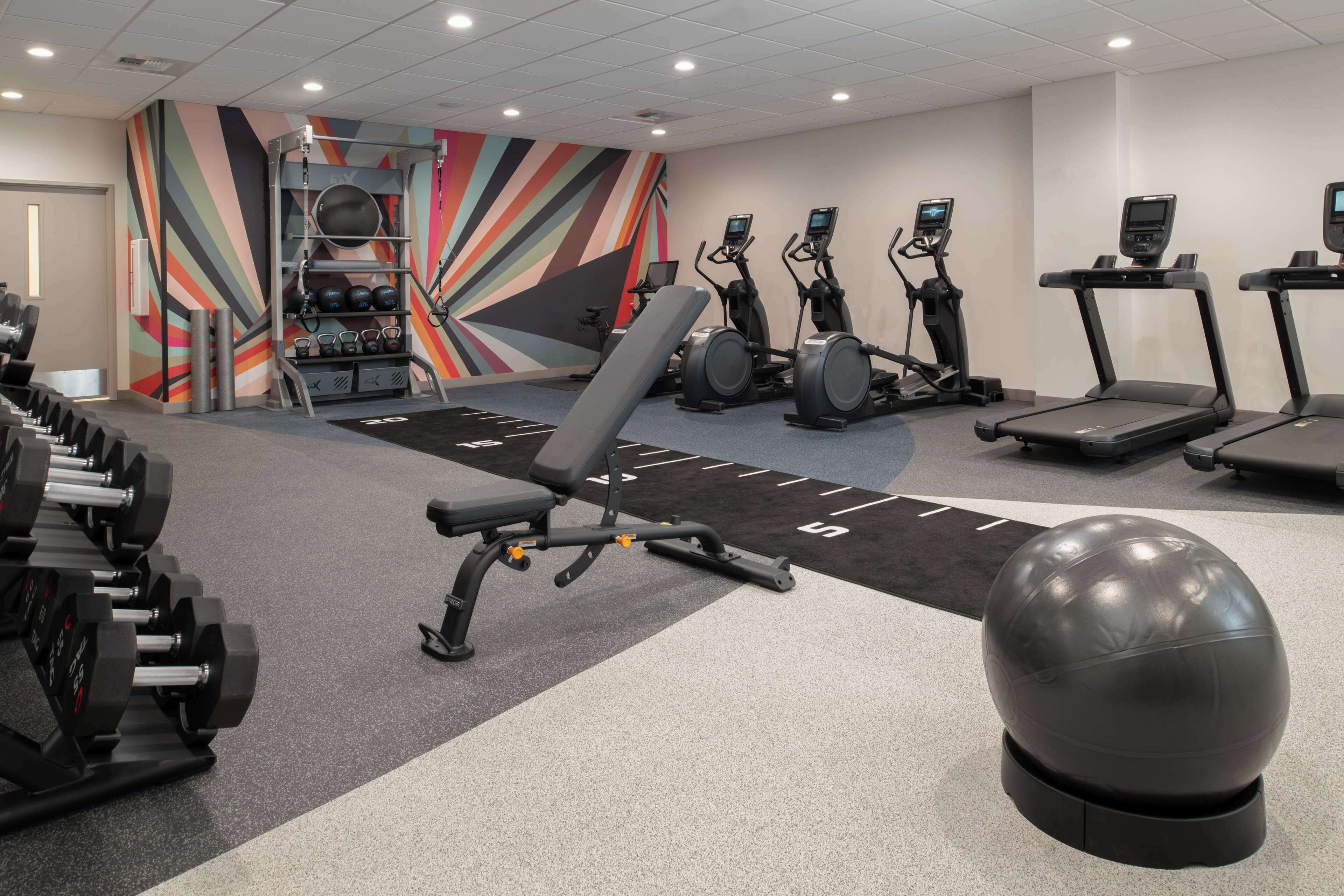 Een fitnessruimte met loopbanden, elliptische trainers, een bankje en gewichten.