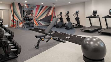 Een fitnessruimte met loopbanden, elliptische trainers, een bankje en gewichten.