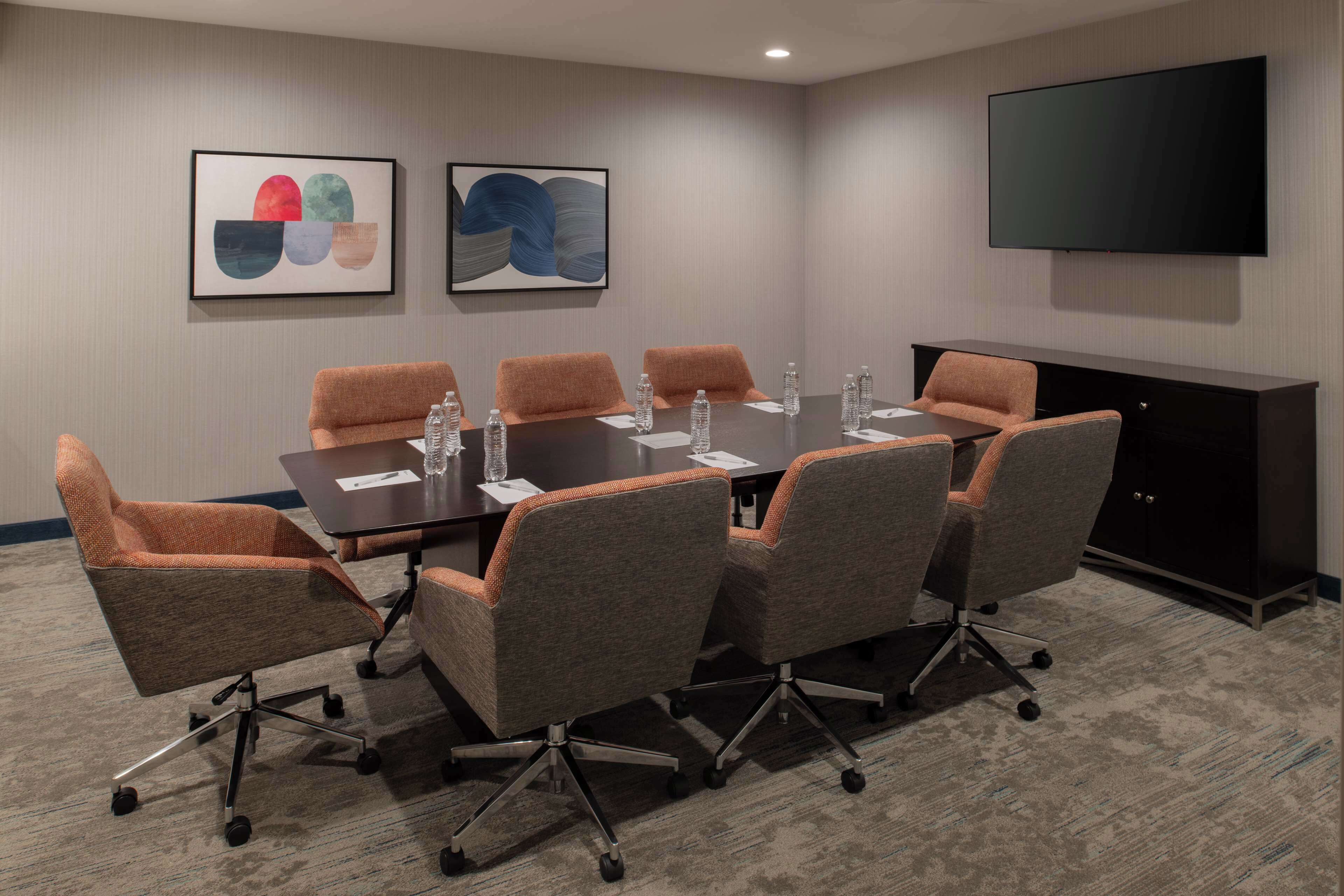 Une salle de conférence avec une longue table, six chaises et un téléviseur fixé au mur.