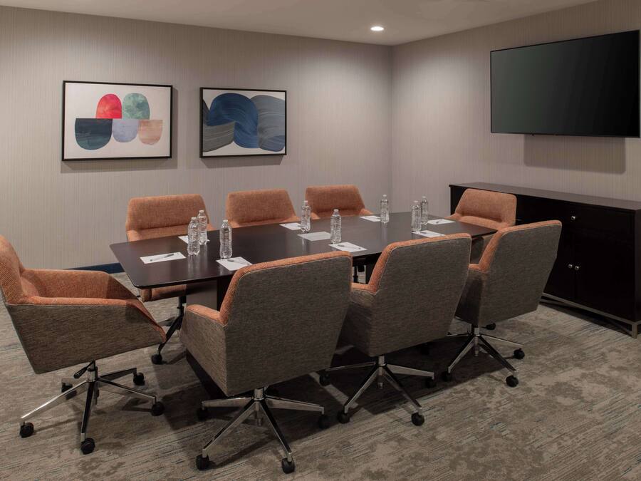Une salle de conférence avec une longue table, six chaises et un téléviseur fixé au mur.