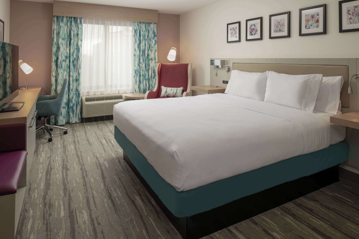 A hotel room with a large bed, a desk with a chair, a TV, and a window with curtains.