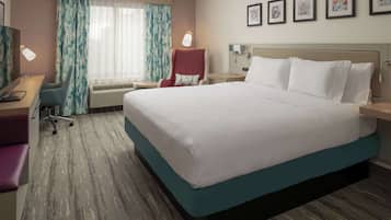A hotel room with a large bed, a desk with a chair, a TV, and a window with curtains.