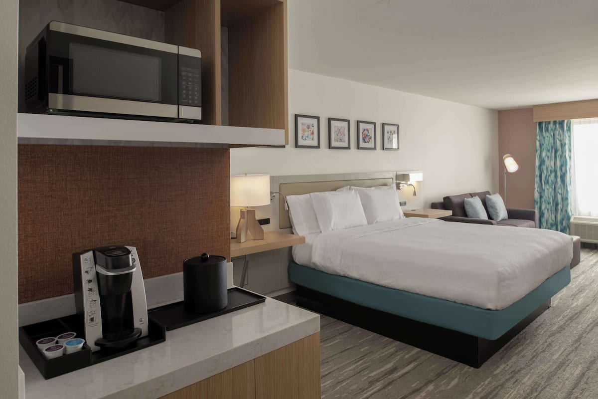 A hotel room with a bed, a coffee maker, a microwave, a nightstand, and framed pictures on the wall.