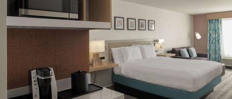 A hotel room with a bed, a coffee maker, a microwave, a nightstand, and framed pictures on the wall.