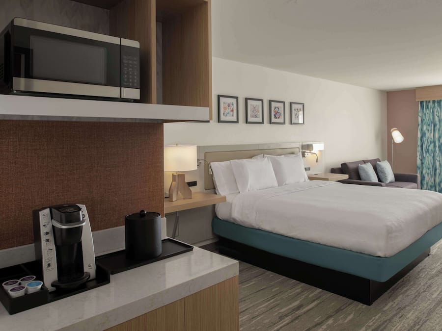 A hotel room with a bed, a coffee maker, a microwave, a nightstand, and framed pictures on the wall.