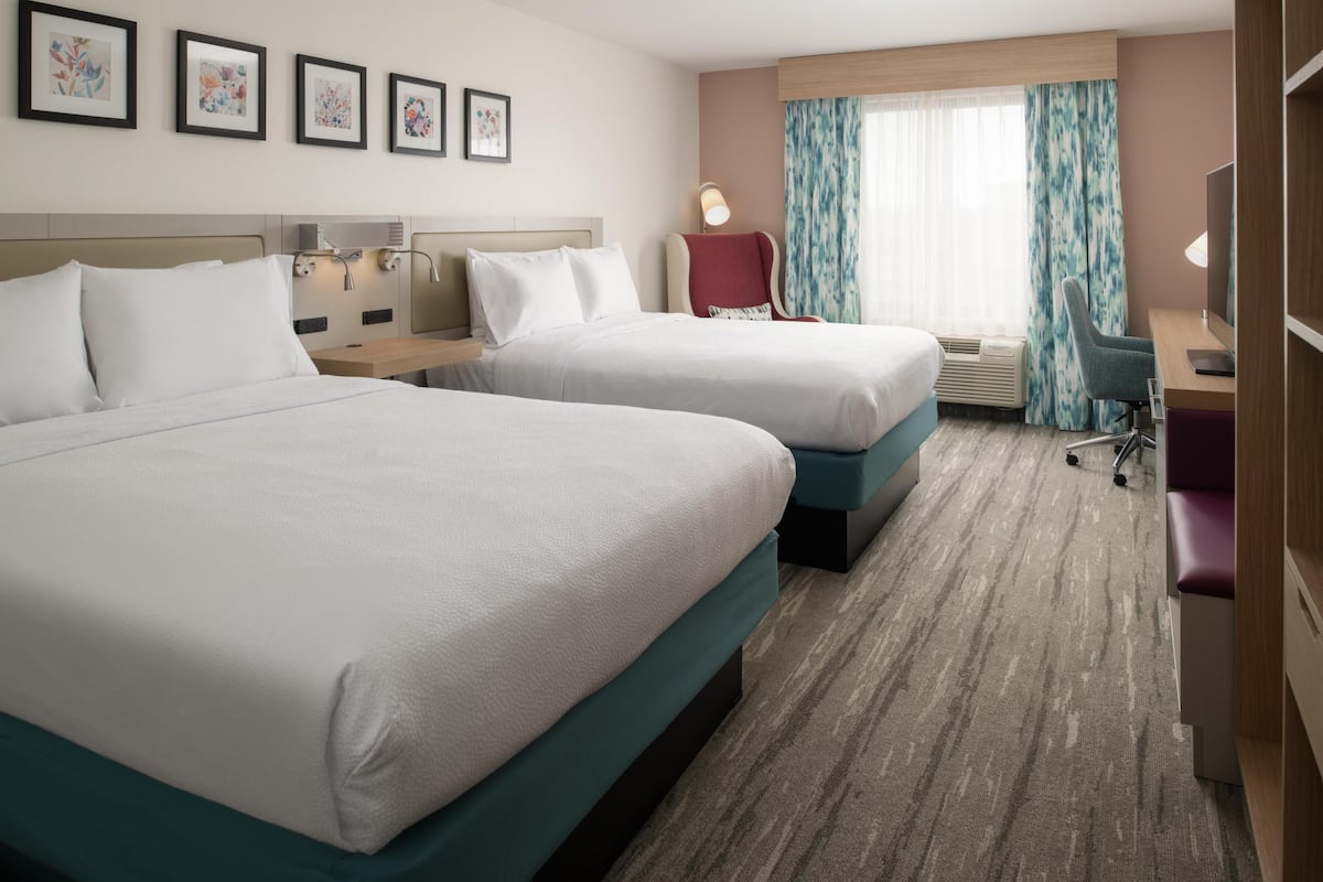 A hotel room with two beds, a desk, a chair, a TV, and a window with curtains.