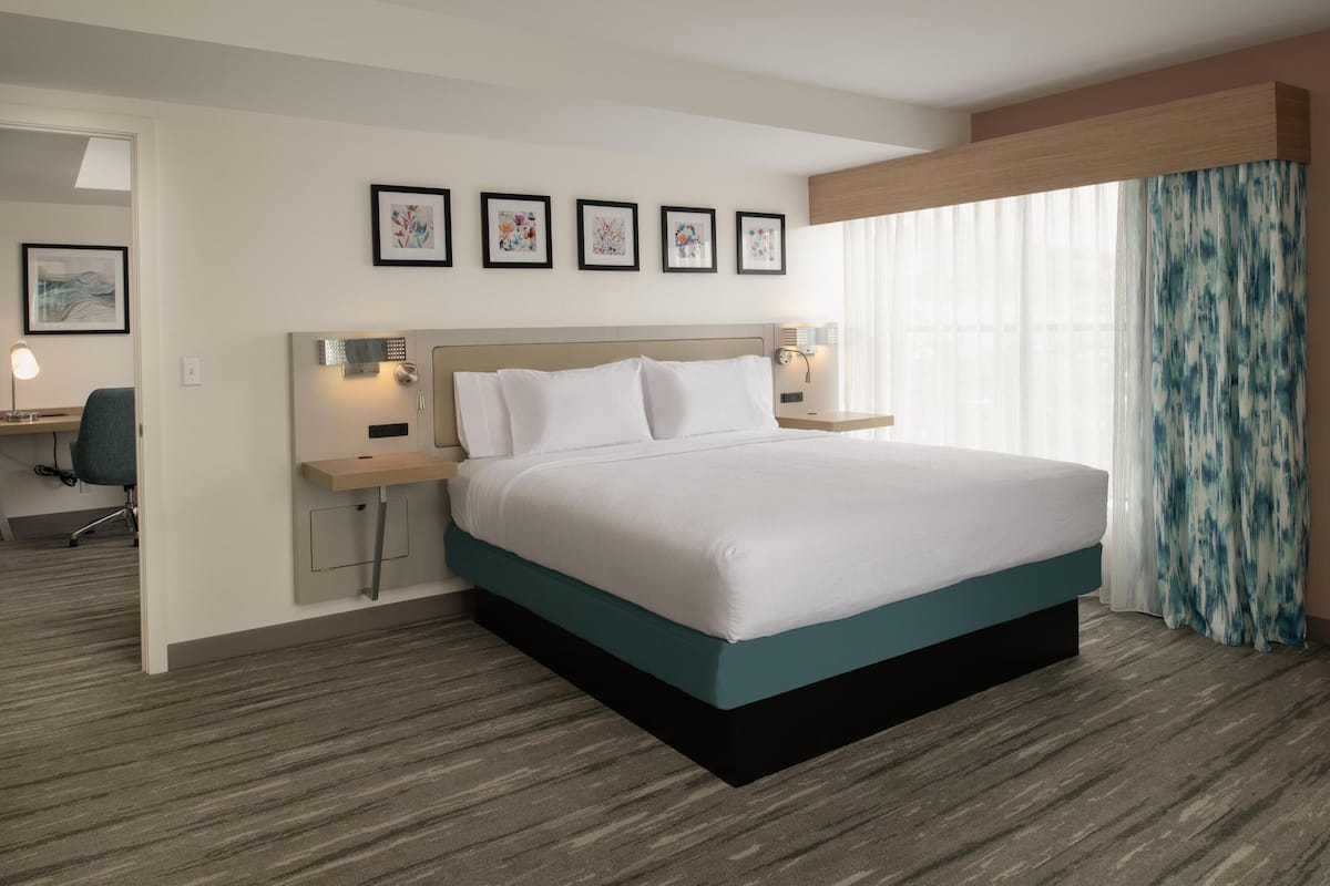 A hotel room with a large bed, a desk with a chair, and a window with curtains.