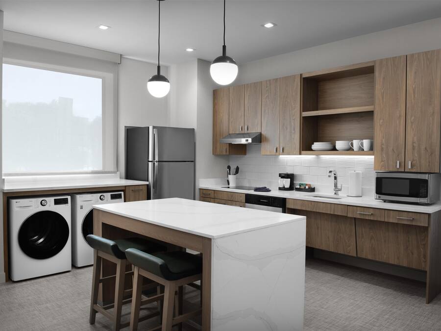 A modern kitchen with wooden cabinets, a built-in washing machine, a large window, and pendant lighting.