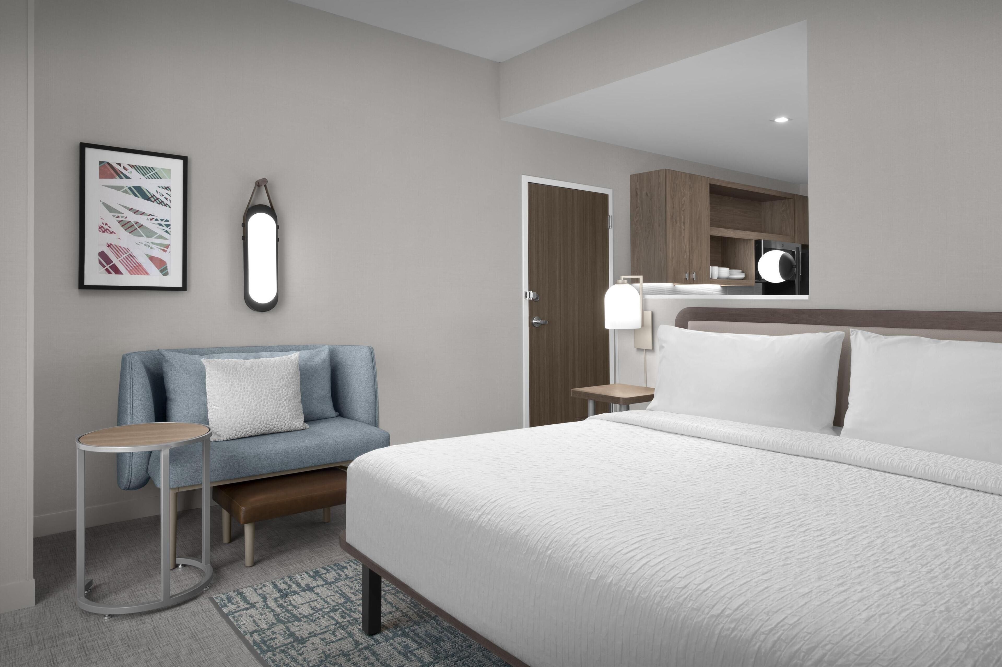 A modern hotel room with a large bed, a blue sofa, a small round table, and a mirror.
