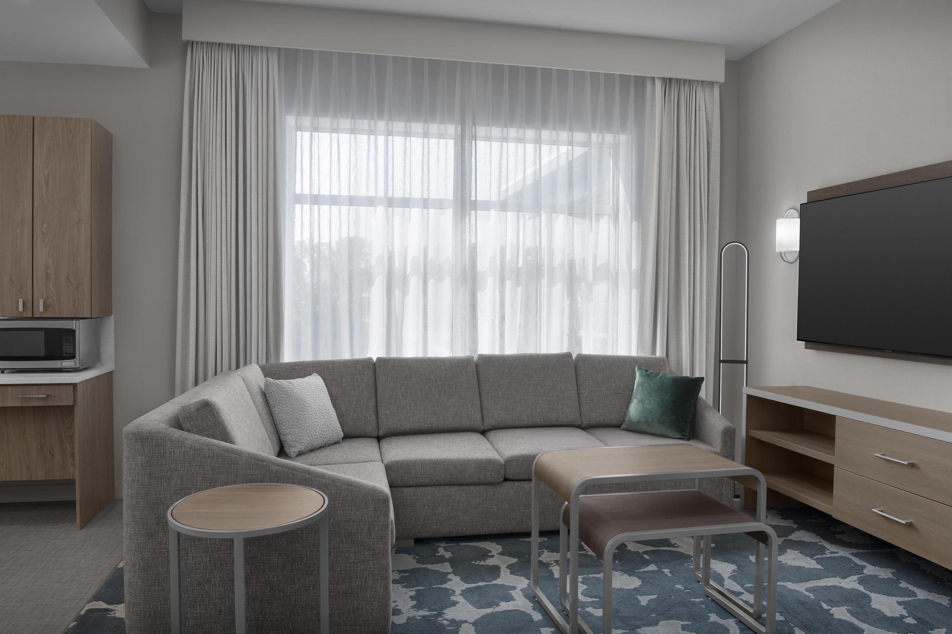 A modern living room with a sectional sofa, a flat-screen TV, a small table, and a cabinet.