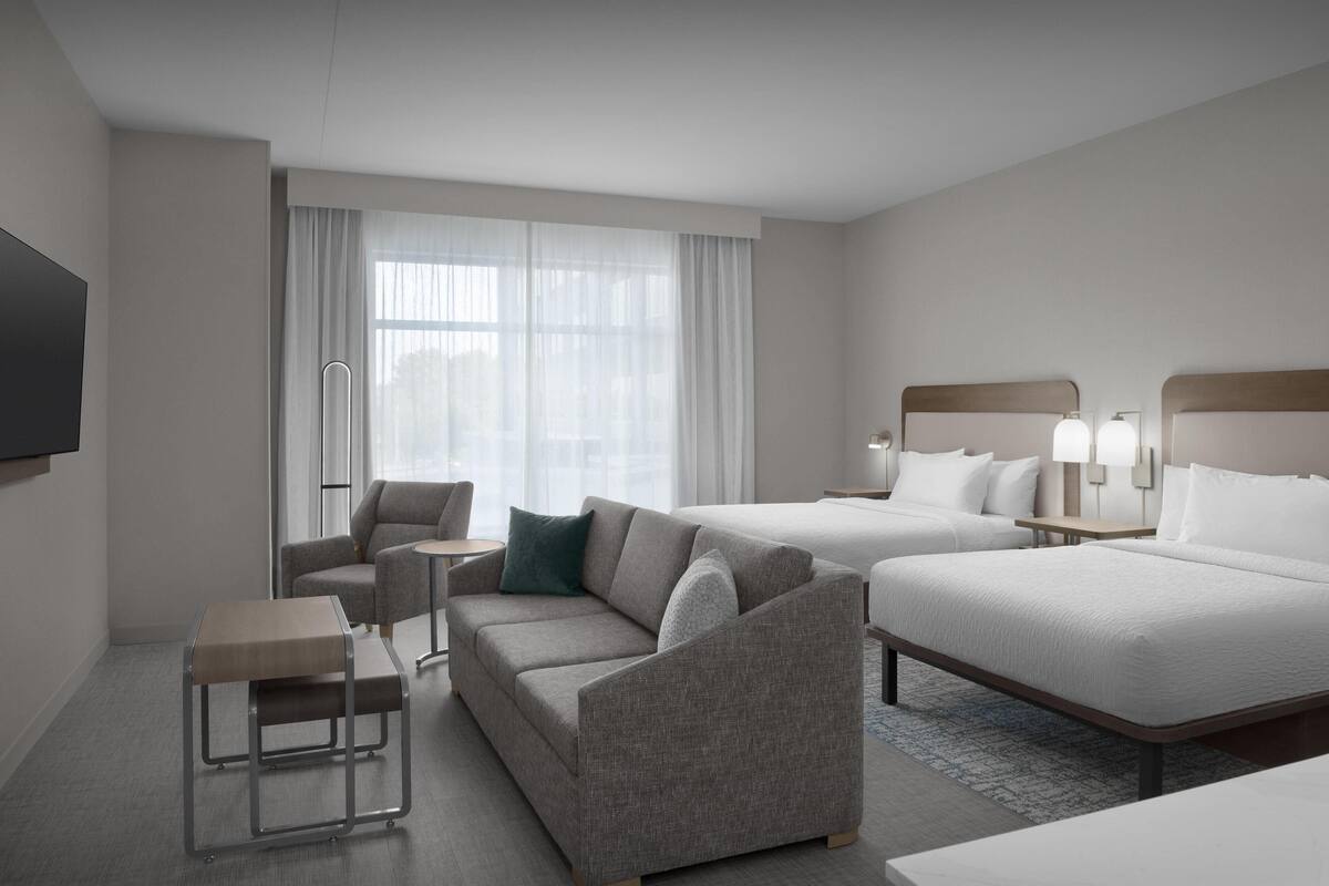 Une chambre d’hôtel équipée d’un canapé, d’une petite table, d’un lit et d’un téléviseur fixé au mur.
