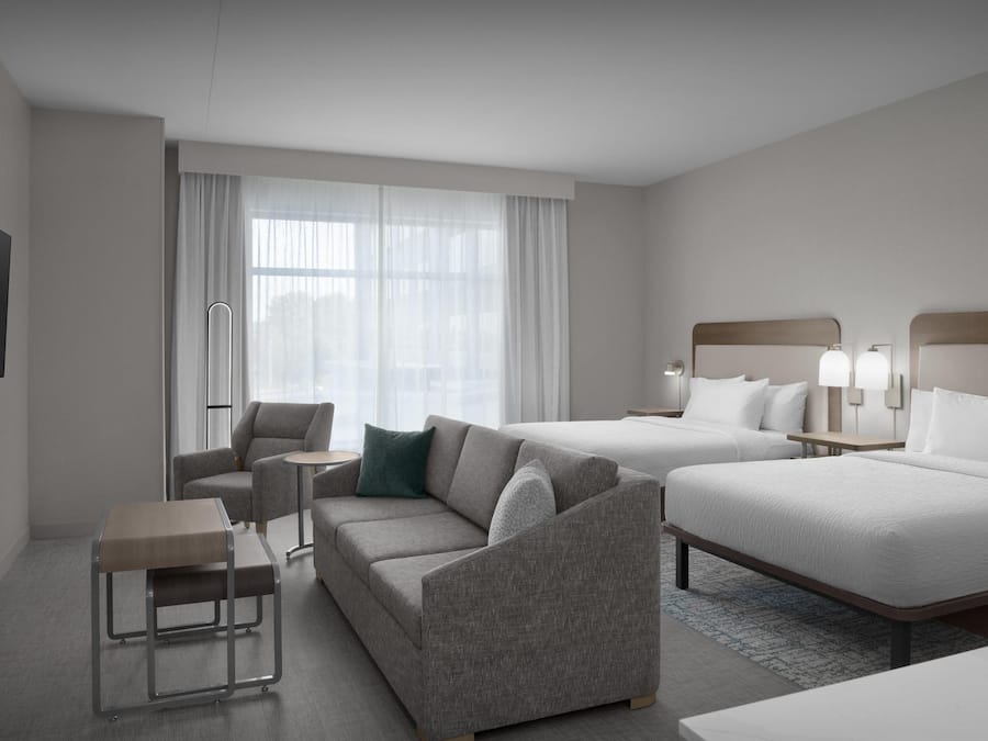 Een hotelkamer met een bank, een klein tafeltje, een bed en een aan de muur bevestigde televisie.