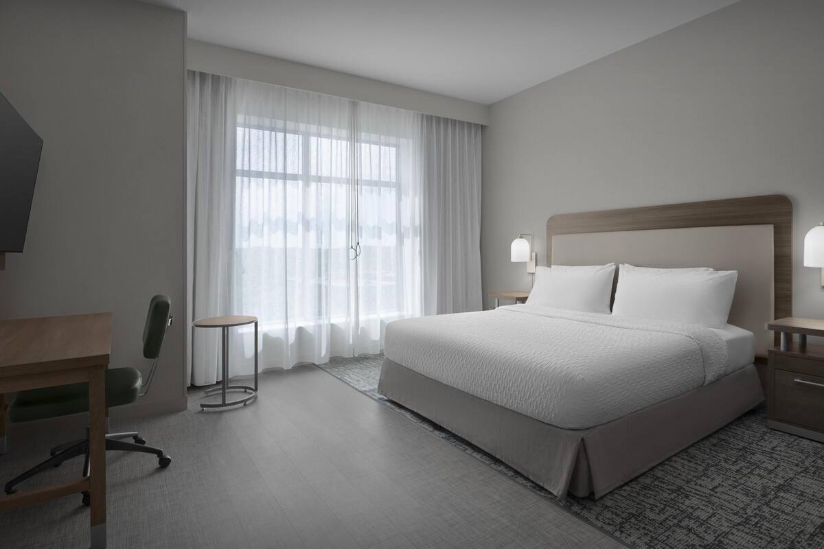 Une chambre d’hôtel avec un grand lit, un bureau, une chaise et une fenêtre avec des rideaux.