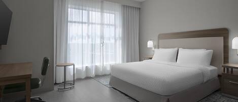 A hotel room with a large bed, a desk, a chair, and a window with curtains.