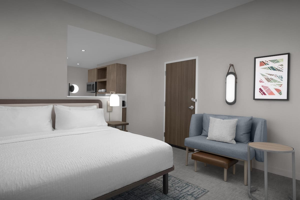 Une chambre d’hôtel moderne dotée d’un grand lit, d’un coin salon avec un banc, d’une petite table, d’une armoire et d’un luminaire fixé au mur.