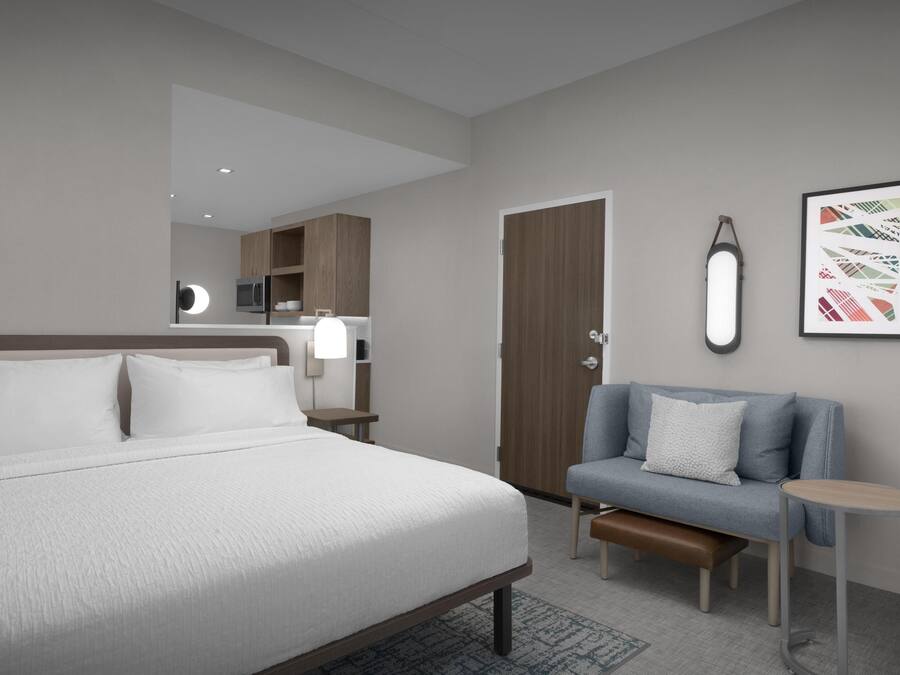 Une chambre d’hôtel moderne dotée d’un grand lit, d’un coin salon avec un banc, d’une petite table, d’une armoire et d’un luminaire fixé au mur.