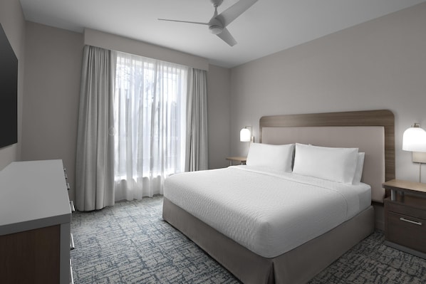 A hotel room with a large bed, a desk, a ceiling fan, and a window with curtains.